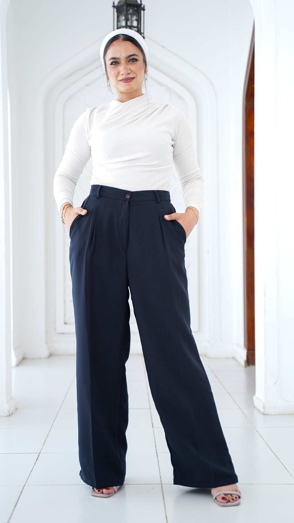 Woman wearing a white top and navy pants with a hijab in a white interior setting